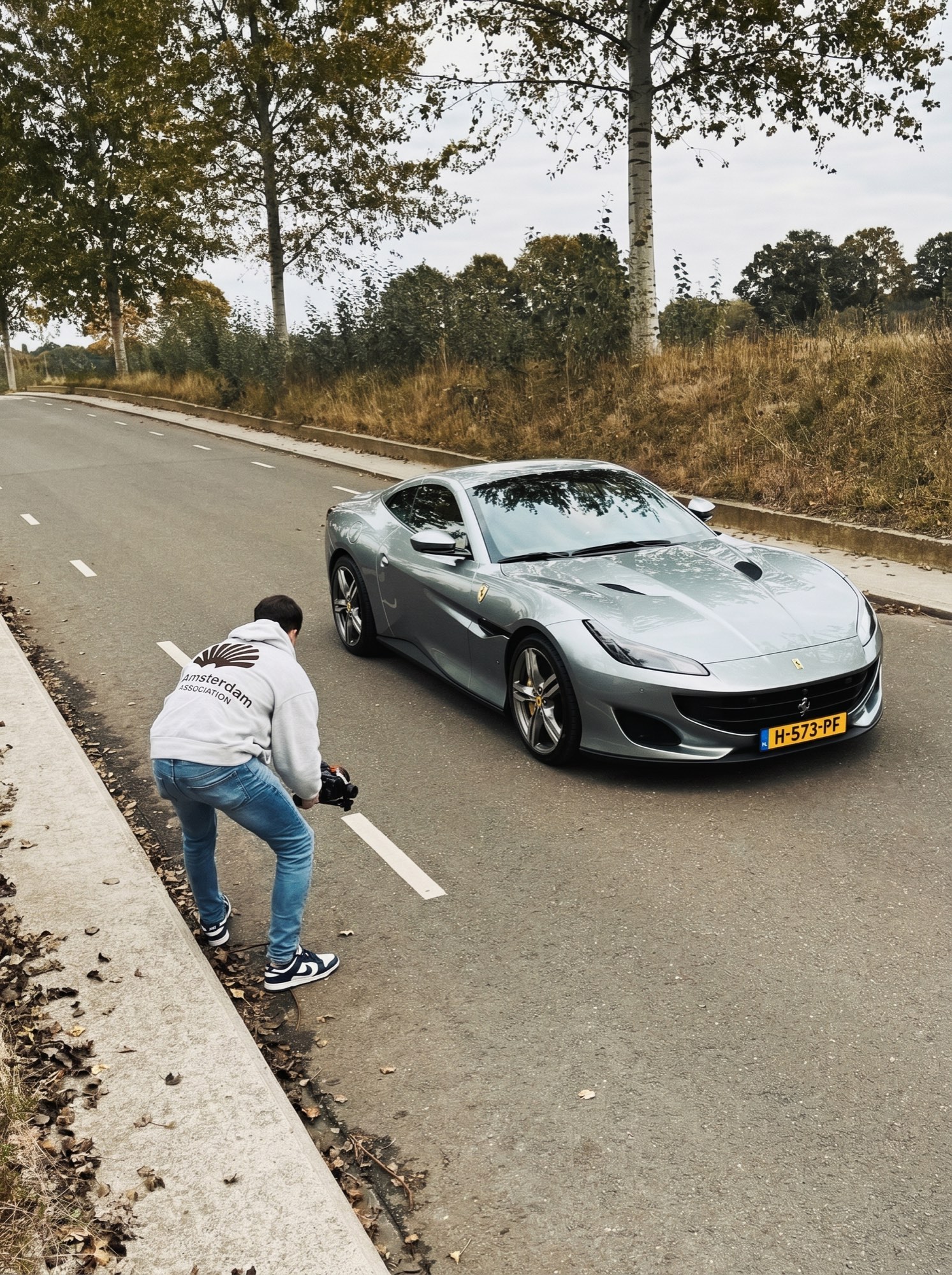 Achter de schermen: cameraman filmt laag bij de grond een zilvergrijze Ferrari op de weg