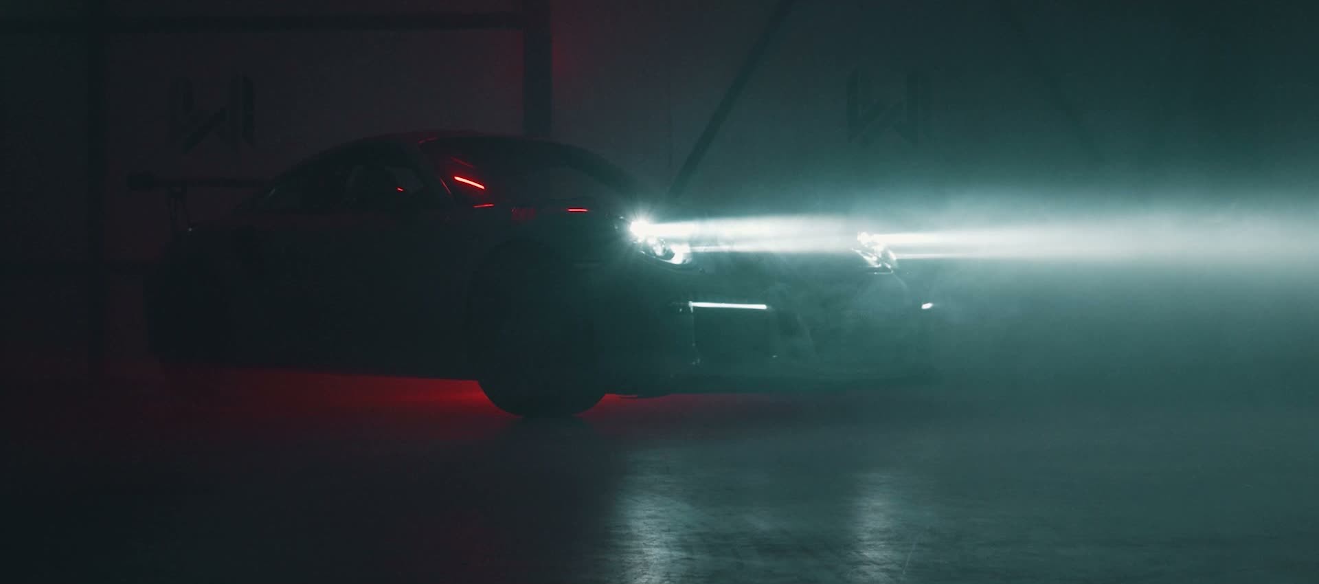 Donkere Porsche met brandende koplampen in een mistige loods met rood licht