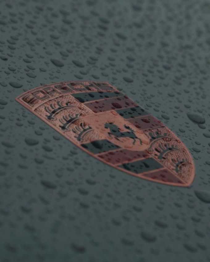 Detail van het Porsche-embleem op de motorkap, met regendruppels