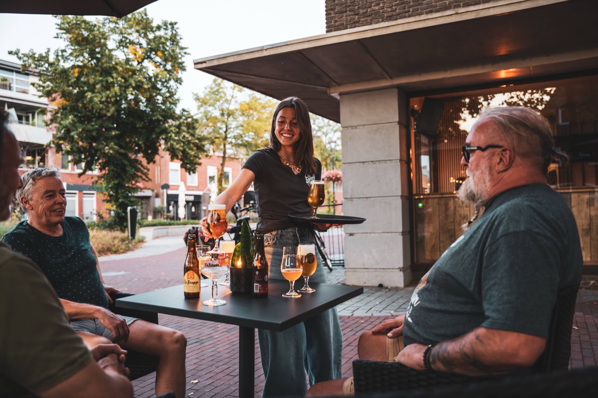 Serveerster brengt bier naar gasten op het terras in de avondzon