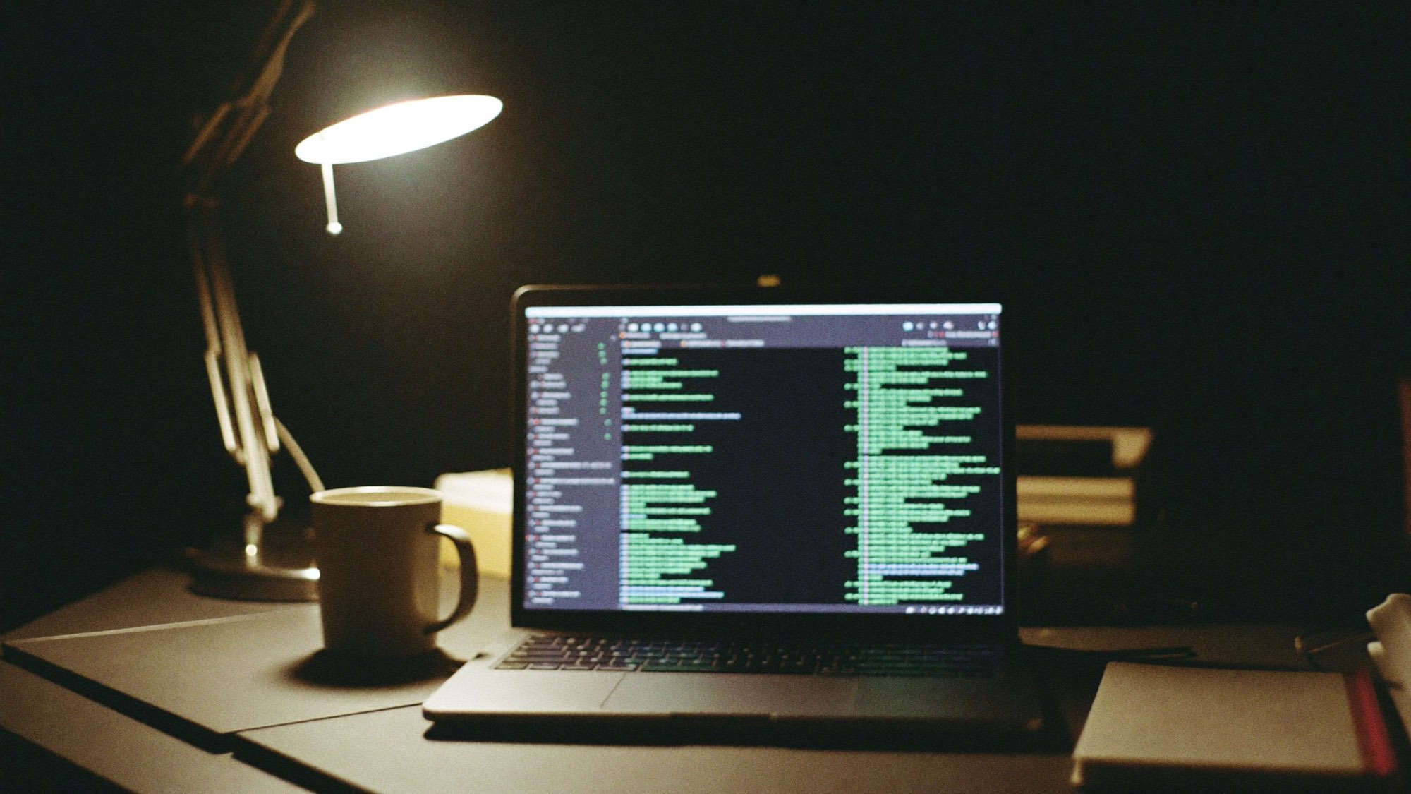 Laptop met code op een bureau in de avond, verlicht door een bureaulamp