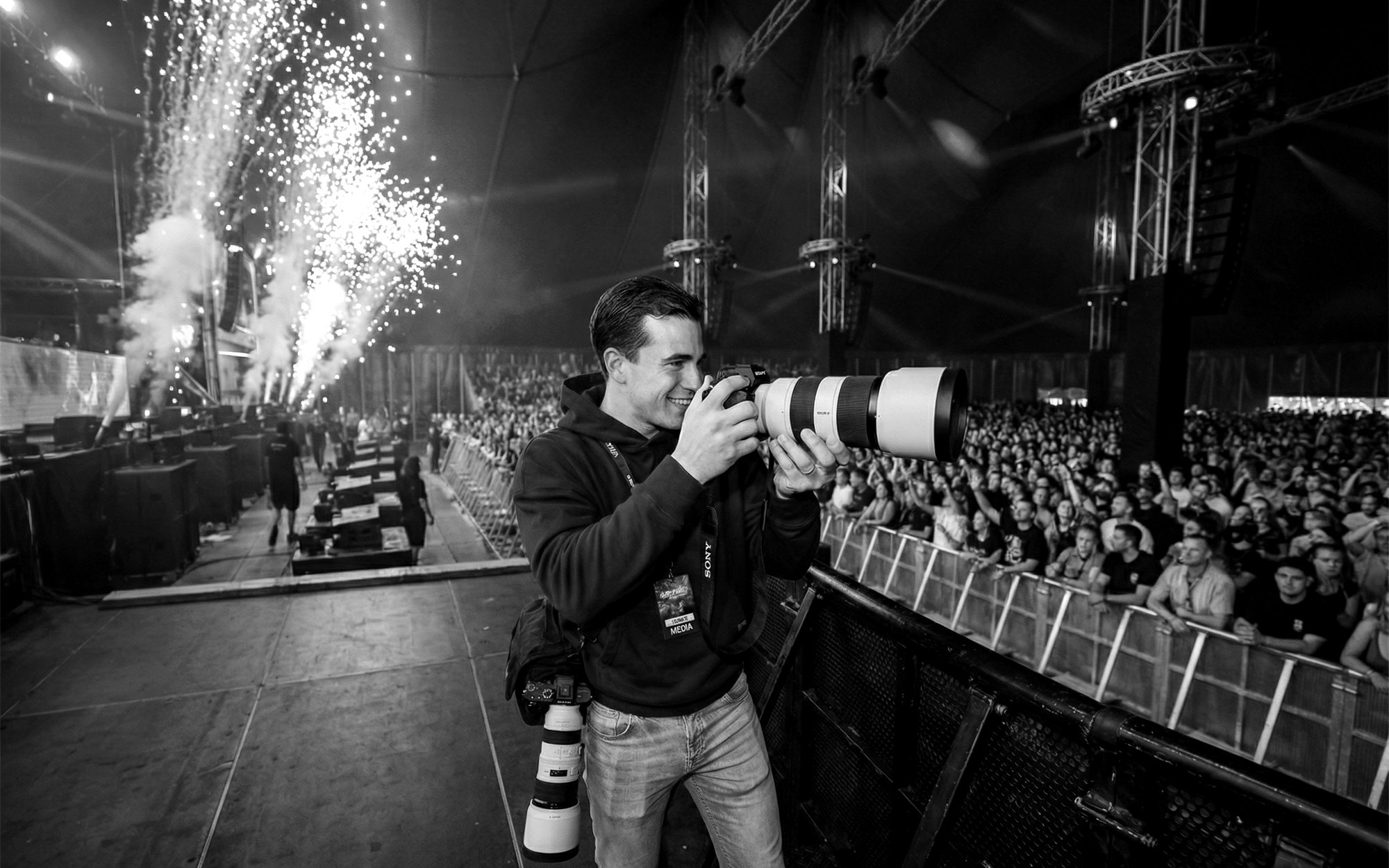 Fotograaf met telelens vooraan bij het podium tijdens een festivalshow met vuurwerk
