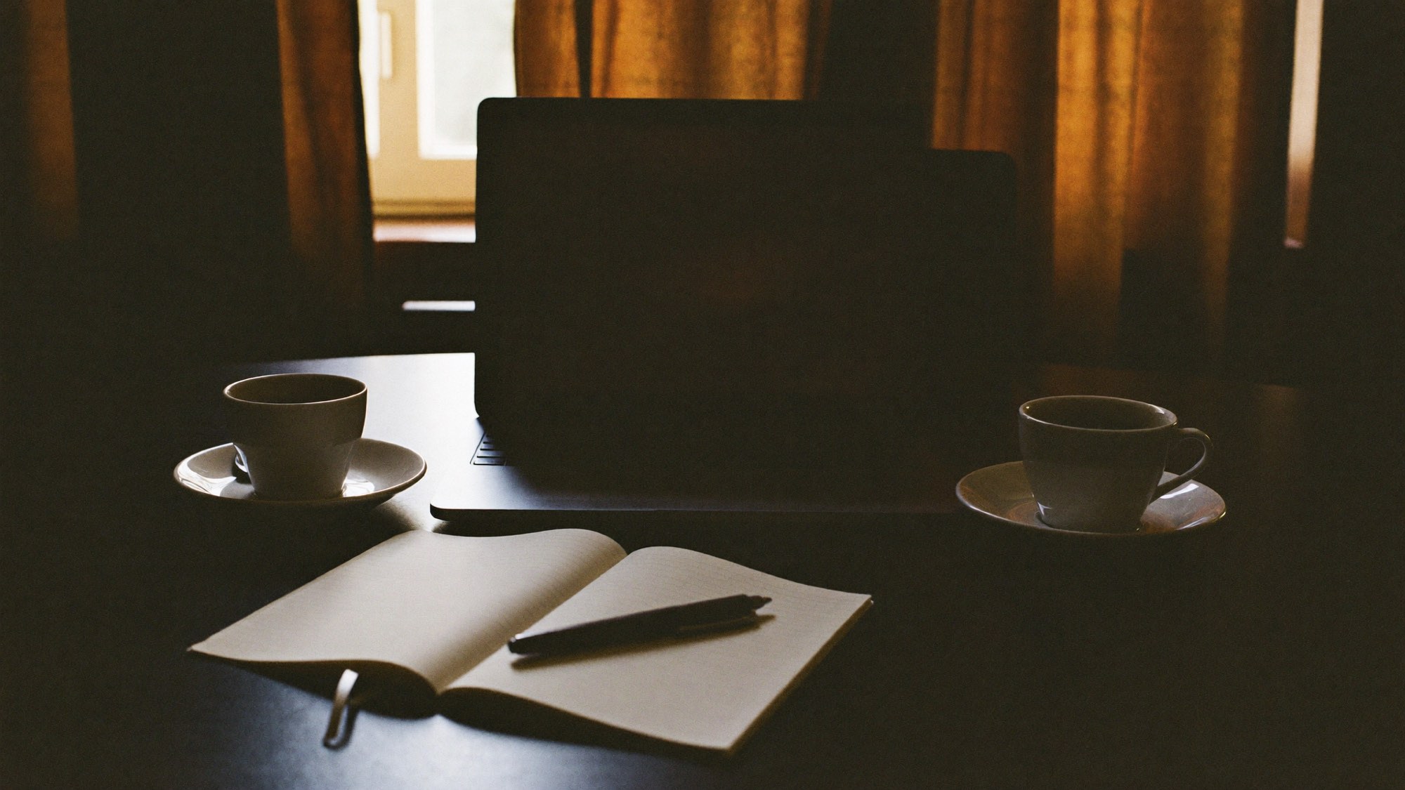 Laptop, twee koppen koffie en een leeg notitieblok op tafel bij de intake