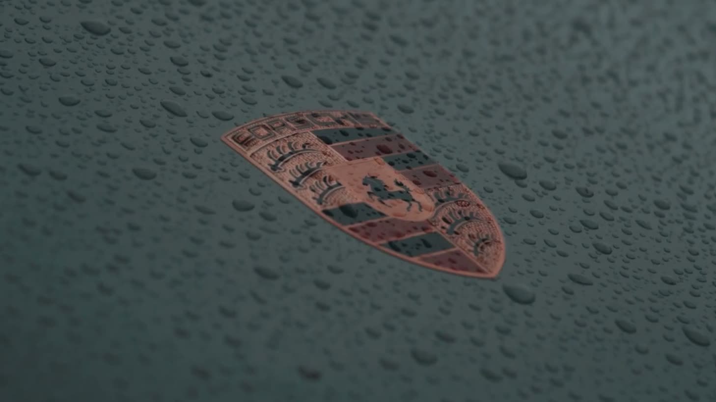 Cinematische still: regendruppels op de motorkap van een Porsche met het embleem in beeld