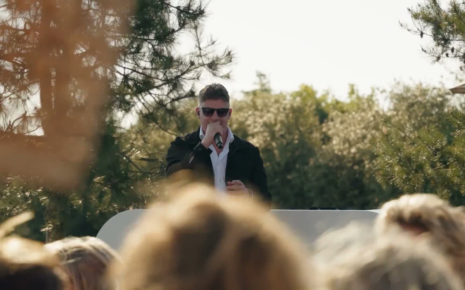 Filmstill van een live-optreden in het gouden avondlicht, zanger met microfoon