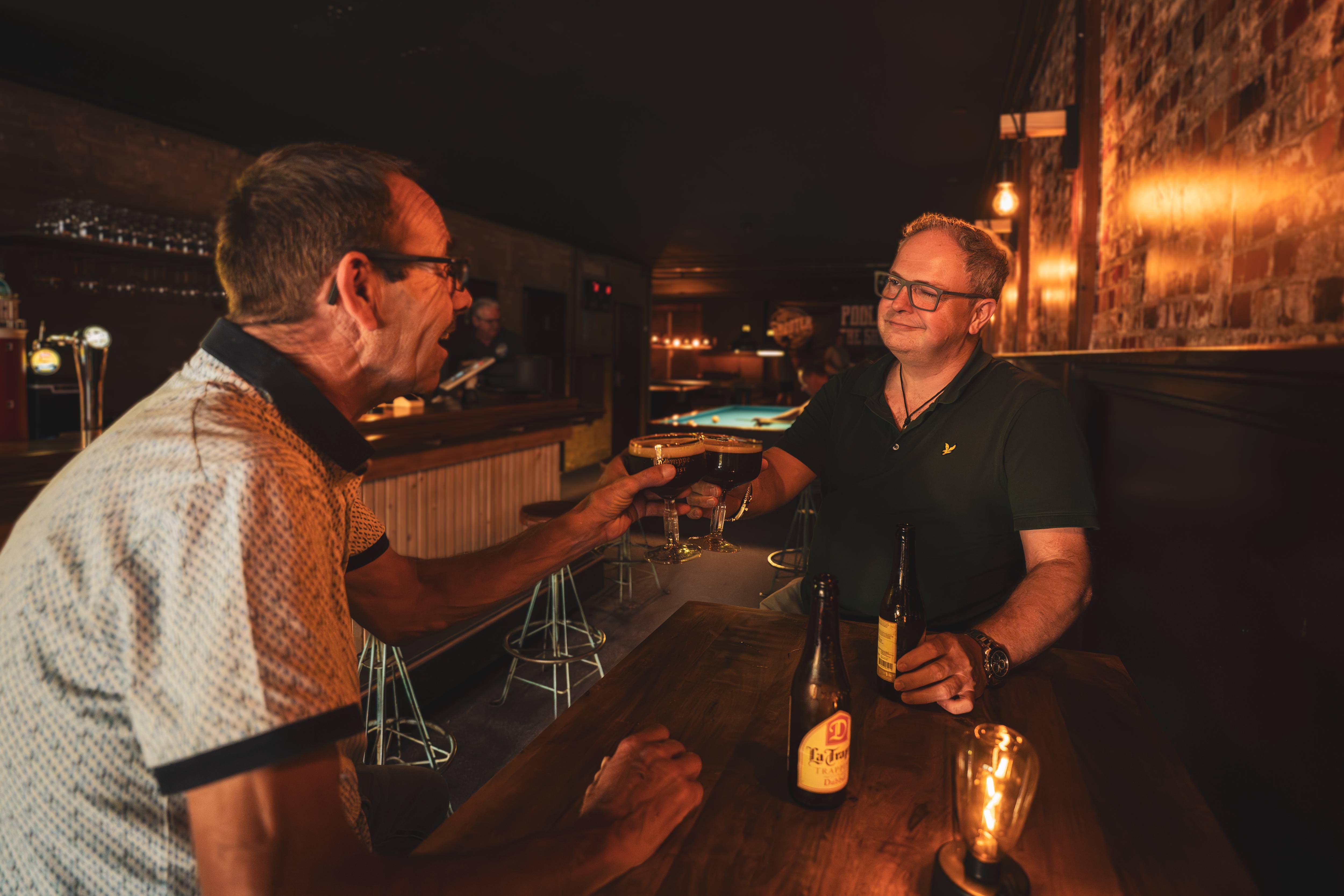 Twee gasten proosten aan de bar met warm licht