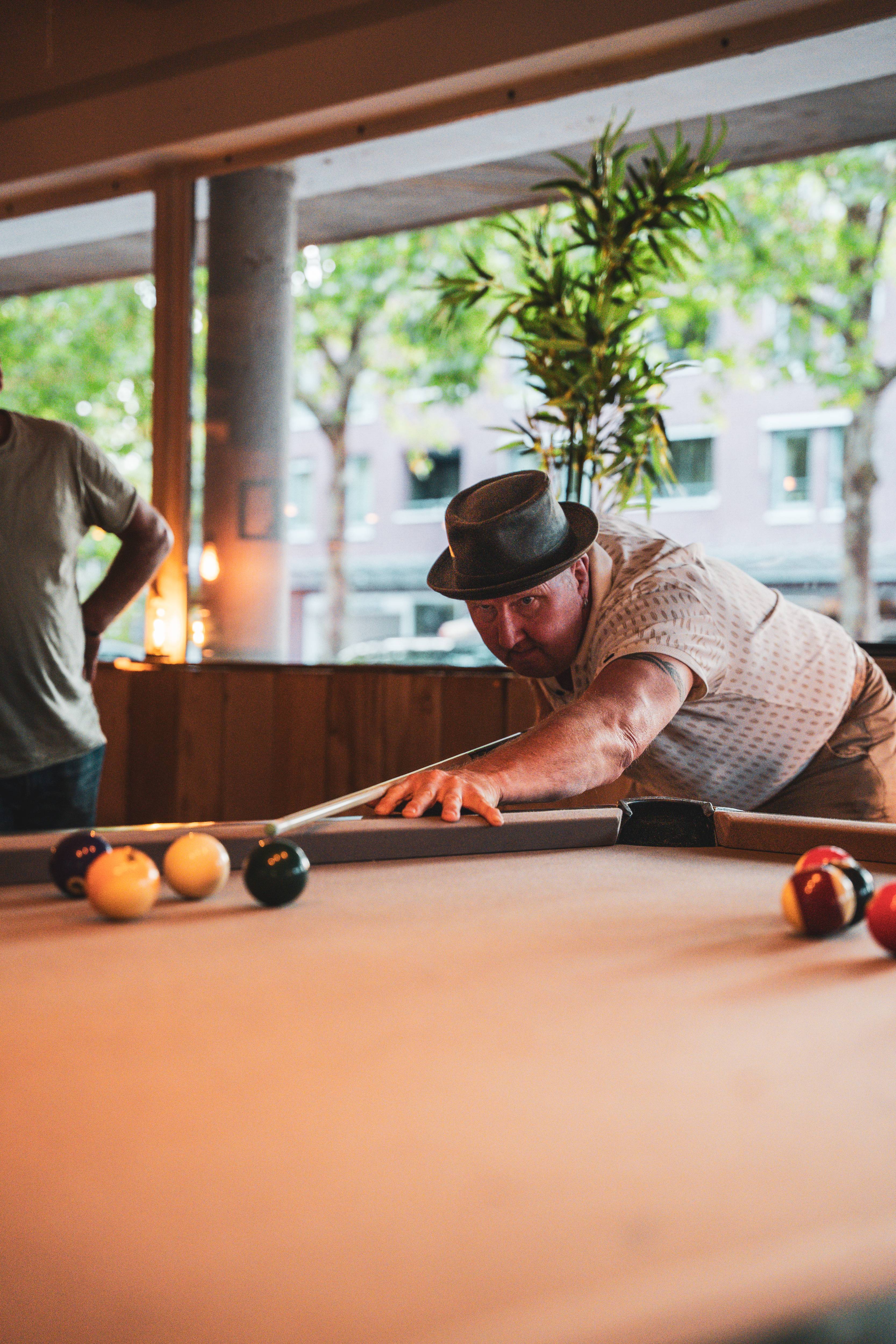 Poolspeler met hoed mikt geconcentreerd op de bal