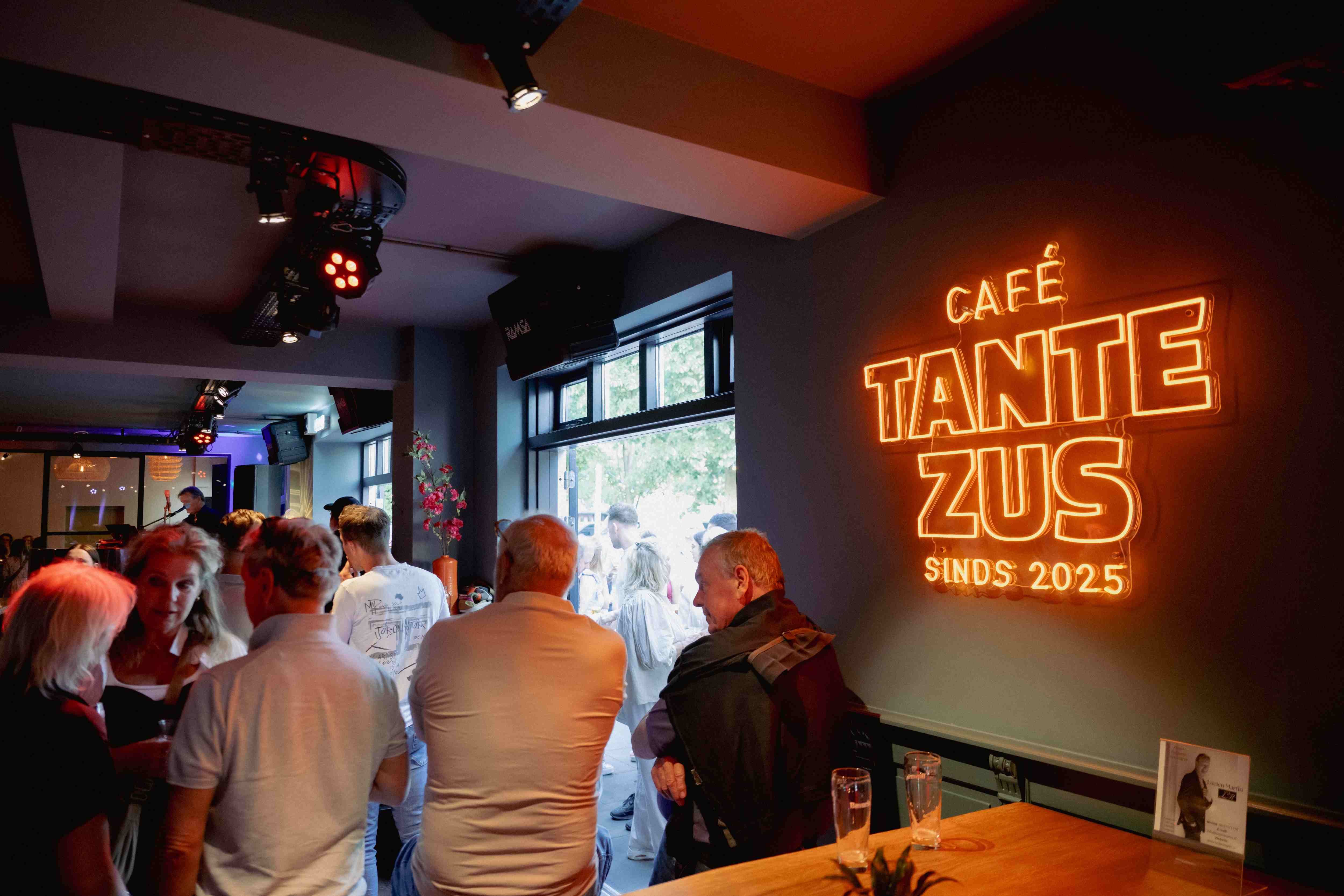 Gasten bij het neon logo van Café Tante Zus